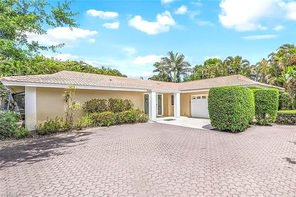 Ranch-style house featuring a garage, a tiled roof, stucco siding, and decorative driveway