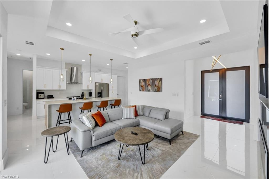 Living area with a tray ceiling, recessed lighting, and a ceiling fan
