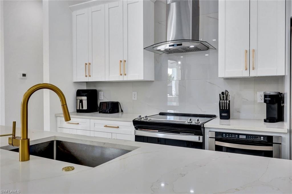 Kitchen with extractor fan, white cabinets, electric stove, and light stone counters