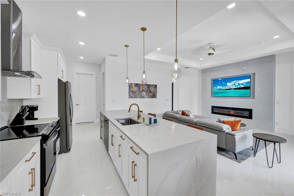 Kitchen featuring range with electric cooktop, white cabinets, wall chimney exhaust hood, hanging light fixtures, and light marble finish floors