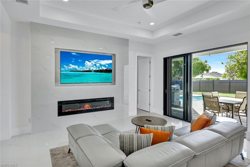 Living area featuring a premium fireplace, recessed lighting, a tray ceiling, and a ceiling fan