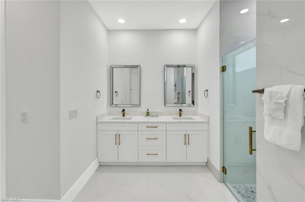 Bathroom featuring a marble finish shower, light marble finish flooring, double vanity, and recessed lighting