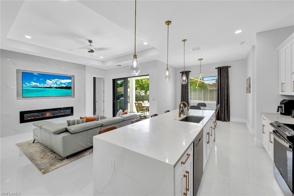 Kitchen featuring white cabinetry, a large island with sink, range, hanging light fixtures, and light stone counters