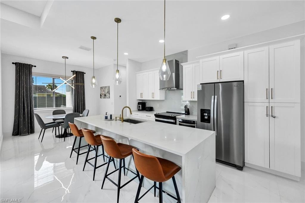 Kitchen featuring stainless steel fridge with ice dispenser, decorative light fixtures, white cabinets, light marble finish flooring, and electric stove