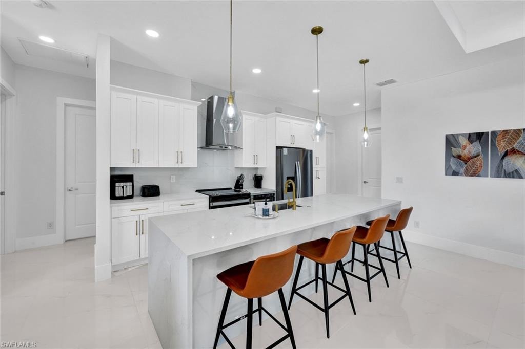 Kitchen featuring tasteful backsplash, wall chimney range hood, pendant lighting, stainless steel fridge, and white cabinets