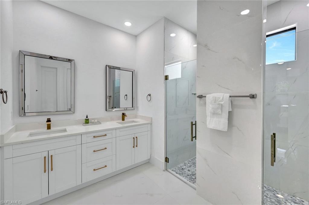Full bathroom with a marble finish shower, double vanity, light marble finish flooring, and recessed lighting
