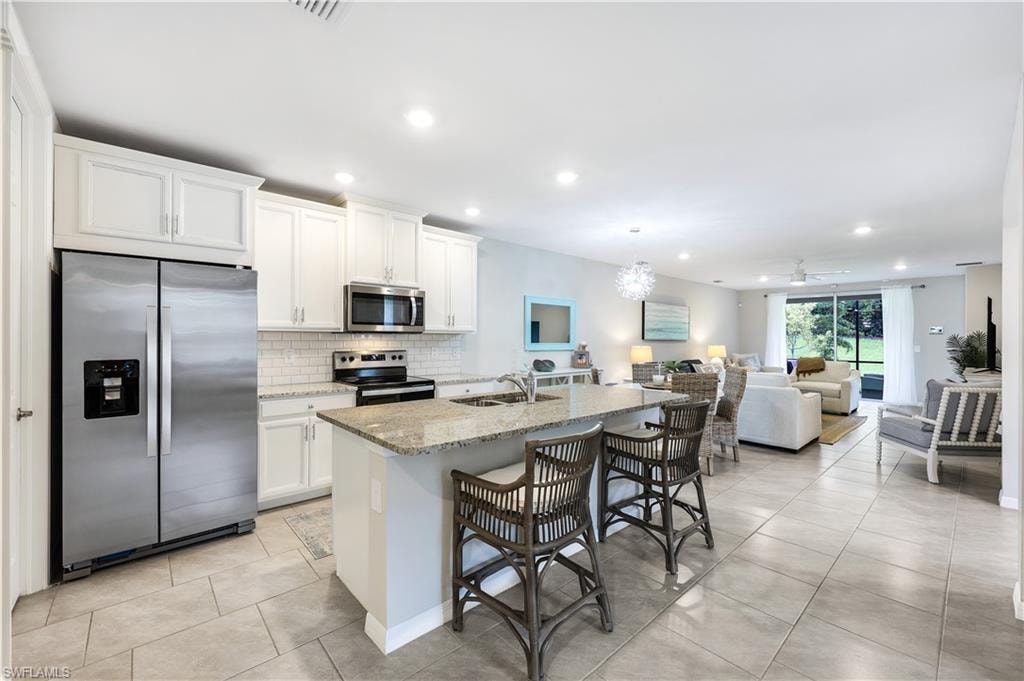 Kitchen featuring appliances with stainless steel finishes, light tile patterned flooring, light stone countertops, a breakfast bar area, and decorative backsplash
