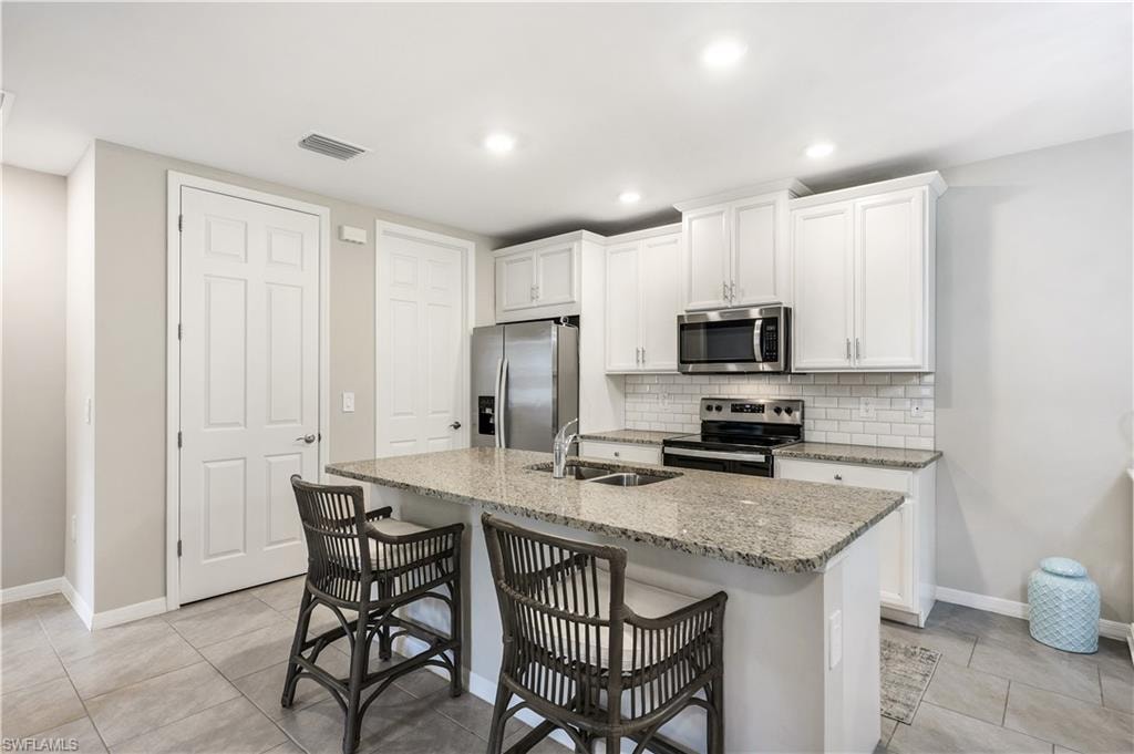 Kitchen featuring light stone counters, stainless steel appliances, white cabinetry, a breakfast bar area, and tasteful backsplash
