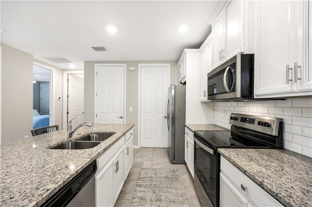 Kitchen with appliances with stainless steel finishes, white cabinets, light stone counters, tasteful backsplash, and light tile patterned floors