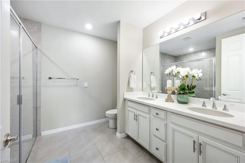Bathroom with double vanity, light tile patterned floors, and a shower stall