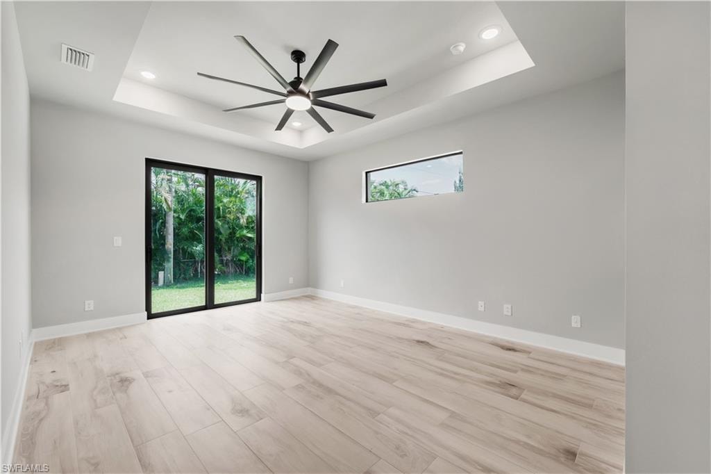 Empty room featuring a tray ceiling, ceiling fan, visible vents, and recessed lighting