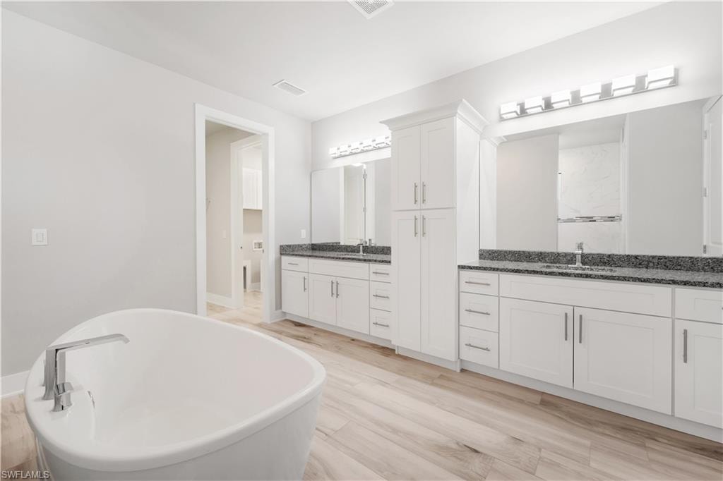 Full bath featuring a freestanding bath, two vanities, a sink, and visible vents