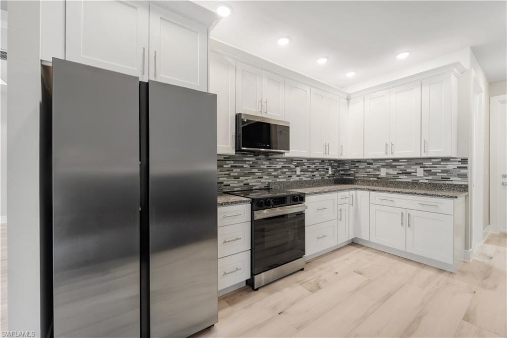 Kitchen with white cabinets, tasteful backsplash, dark stone countertops, and appliances with stainless steel finishes