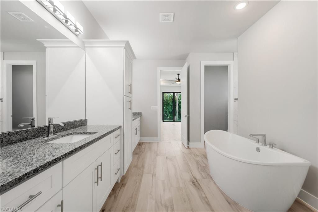 Full bathroom with two vanities, a freestanding tub, visible vents, a sink, and baseboards
