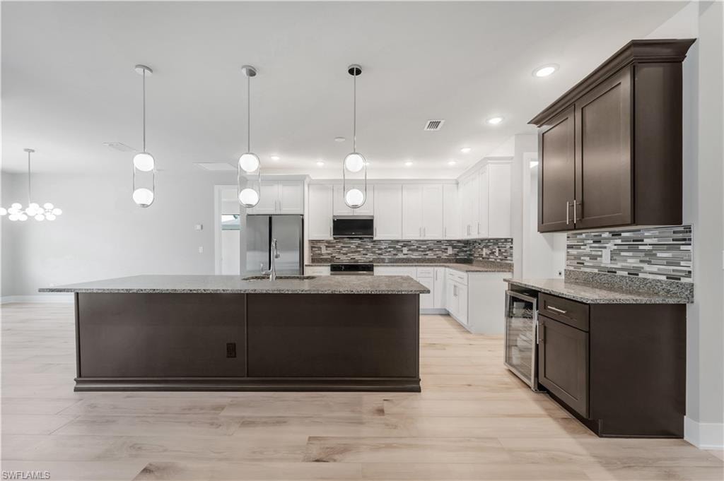 Kitchen featuring dark brown cabinets, tasteful backsplash, appliances with stainless steel finishes, and beverage cooler
