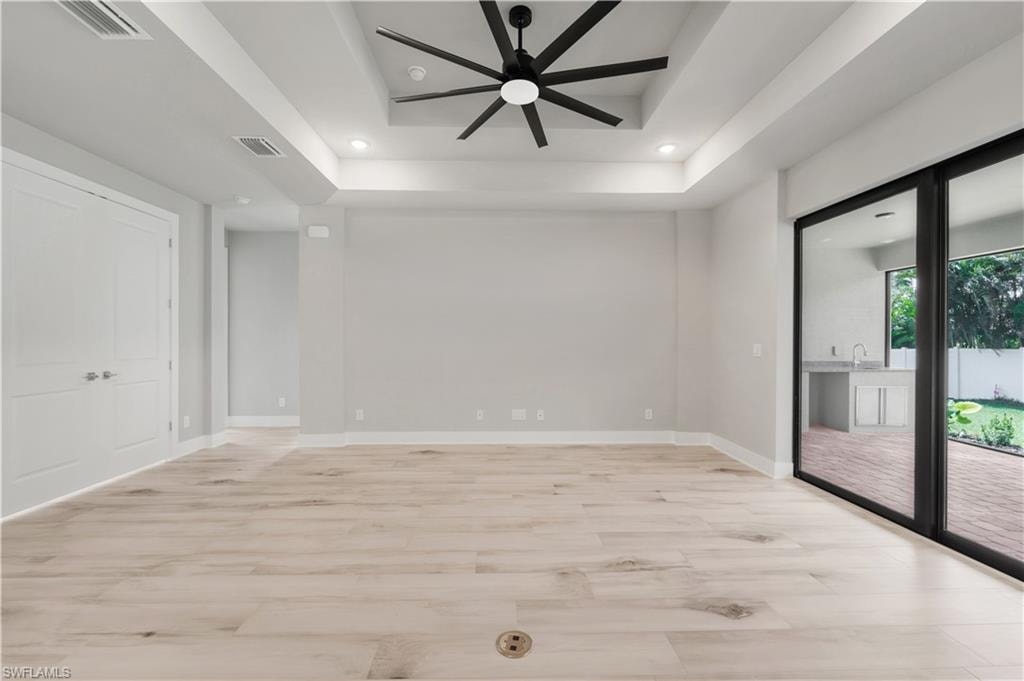 Empty room with a tray ceiling, light wood-type flooring, a ceiling fan, and visible vents