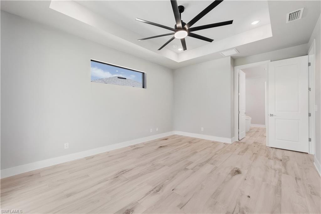 Unfurnished bedroom featuring visible vents, baseboards, a tray ceiling, recessed lighting, and light wood-style flooring