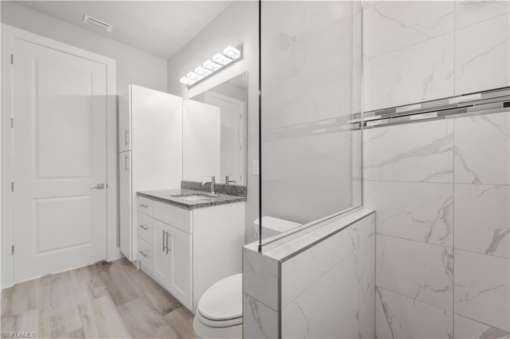Bathroom featuring visible vents, toilet, vanity, and walk in shower