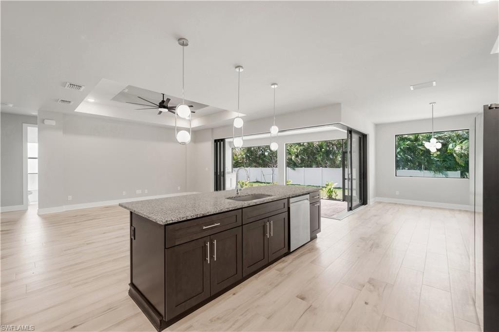 Kitchen with stainless steel dishwasher, open floor plan, baseboards, and a sink