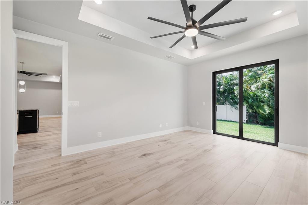 Empty room featuring ceiling fan, a tray ceiling, light wood-type flooring, recessed lighting, and baseboards