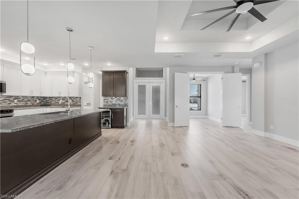Kitchen with tasteful backsplash, a raised ceiling, a ceiling fan, wine cooler, and a sink