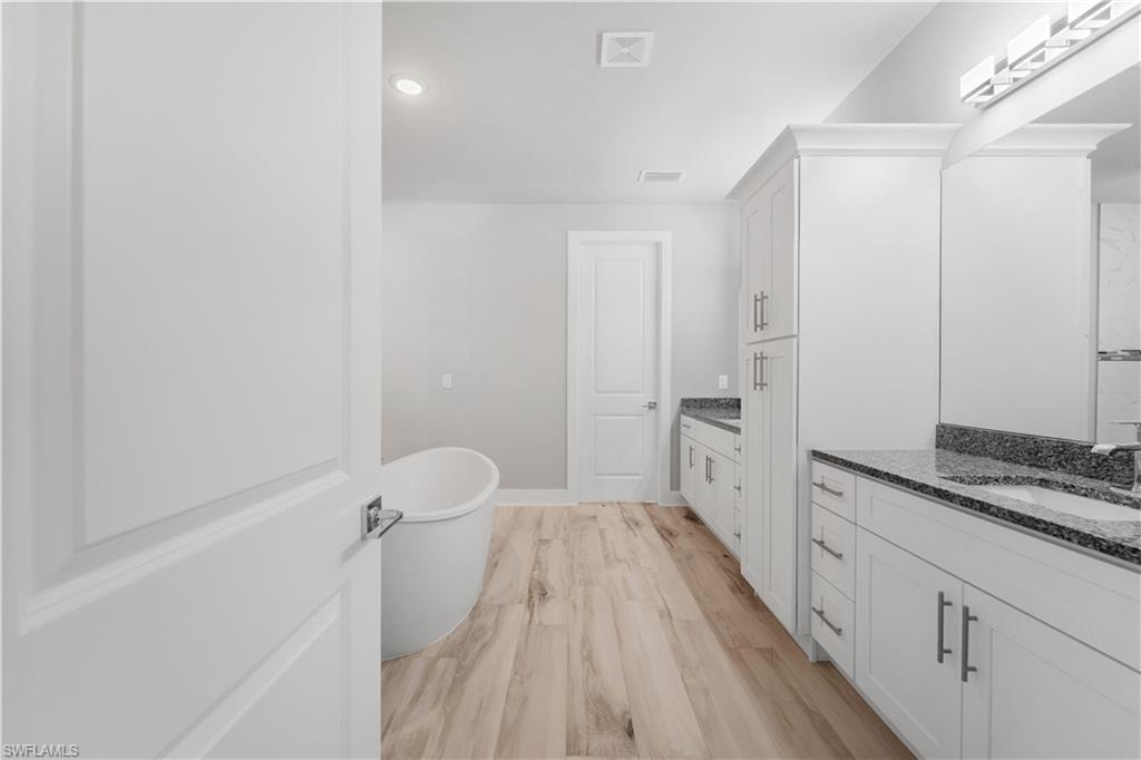 Full bath featuring two vanities, visible vents, a sink, a freestanding bath, and baseboards