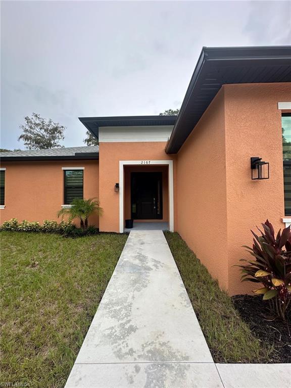 Doorway to property featuring stucco siding and a lawn