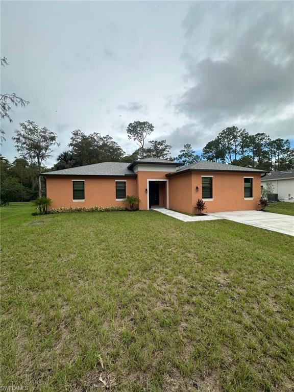 View of front of house featuring stucco siding, a front yard, and driveway