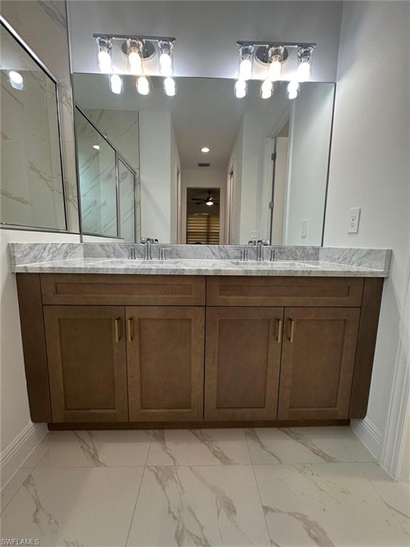 Bathroom featuring light marble finish flooring, double vanity, a marble finish shower, and a ceiling fan