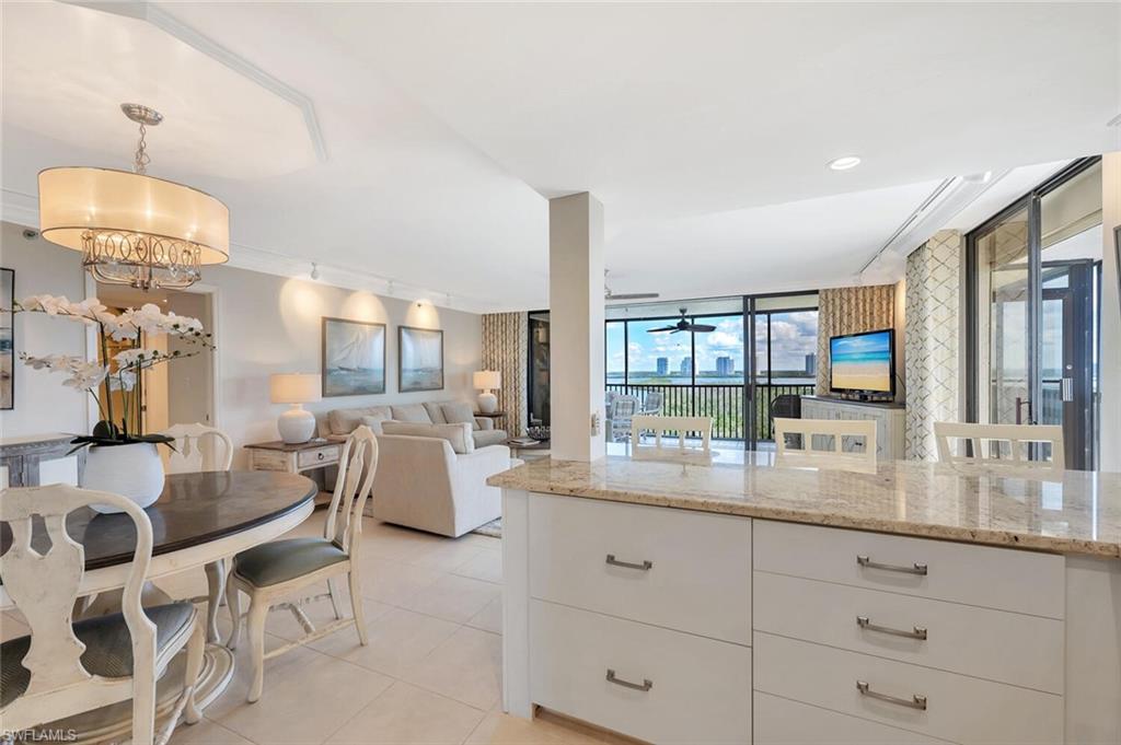 Kitchen with light stone counters, white cabinets, open floor plan, light tile patterned floors, and pendant lighting
