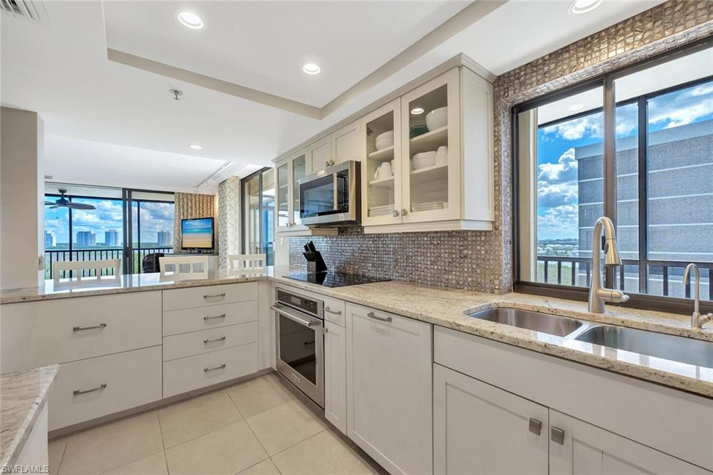 Kitchen featuring backsplash, light stone counters, white cabinets, glass insert cabinets, and stainless steel appliances