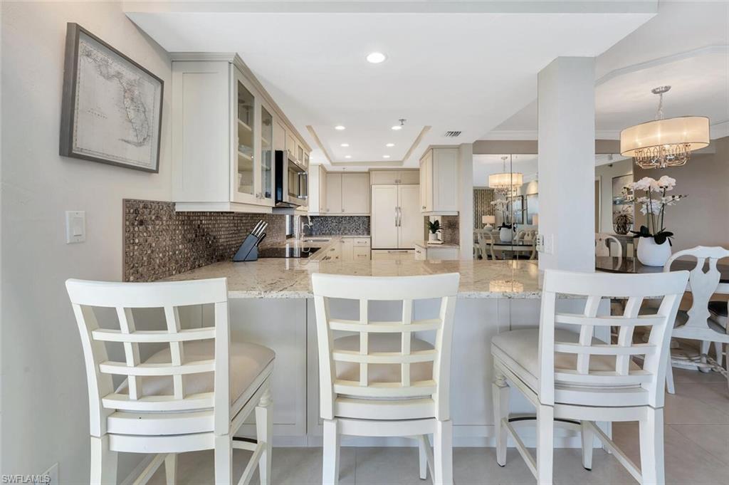 Kitchen with backsplash, light stone countertops, a peninsula, paneled fridge, and recessed lighting