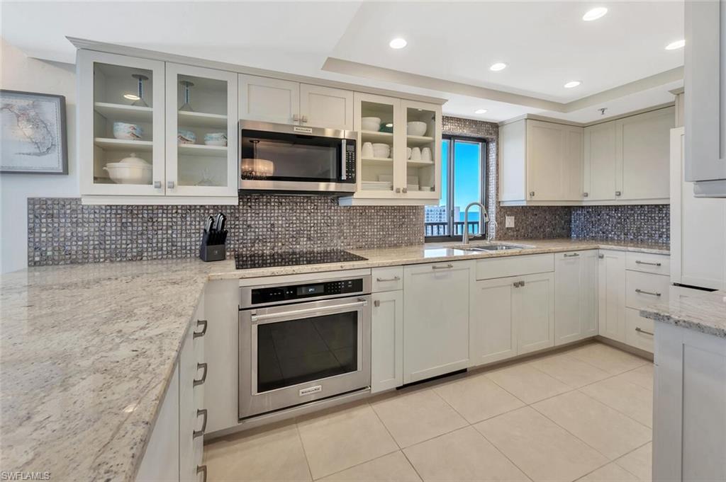 Kitchen with appliances with stainless steel finishes, light stone countertops, backsplash, light tile patterned floors, and a raised ceiling