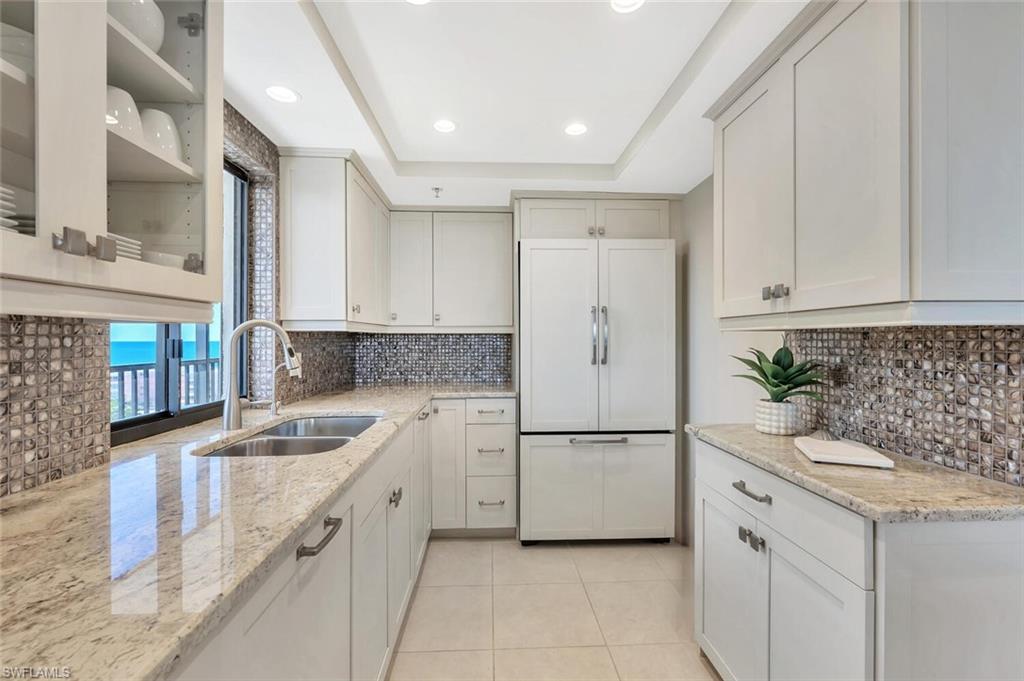 Kitchen with light stone countertops, paneled built in fridge, light tile patterned flooring, recessed lighting, and a raised ceiling