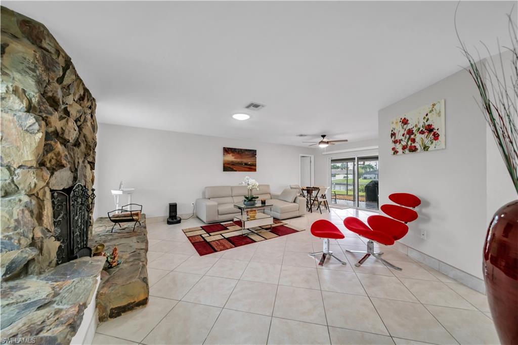 Living area featuring light tile patterned flooring, a ceiling fan, and a stone fireplace