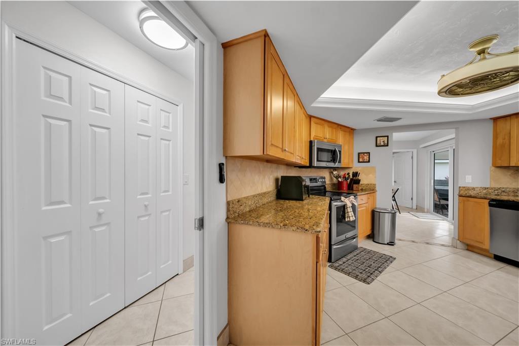 Kitchen with light tile patterned floors, light stone counters, stainless steel appliances, and a tray ceiling