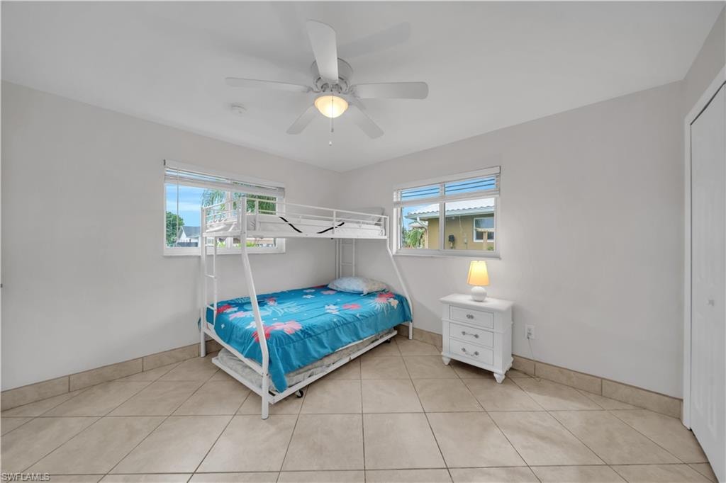 Bedroom with light tile patterned flooring, multiple windows, and a ceiling fan
