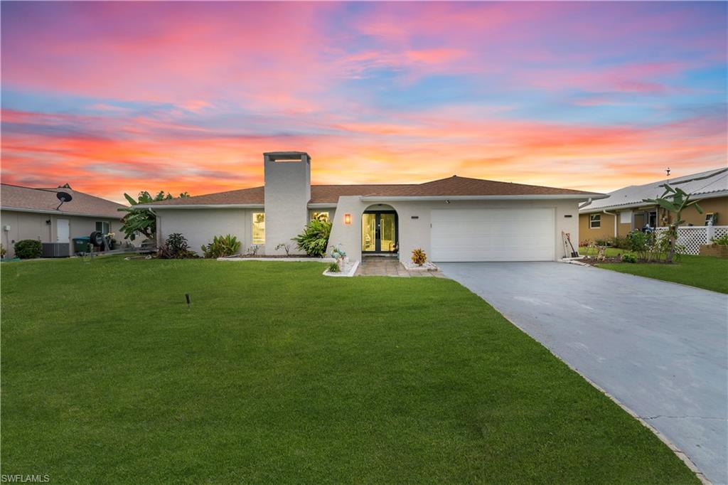 Ranch-style home featuring driveway, stucco siding, an attached garage, a lawn, and a chimney