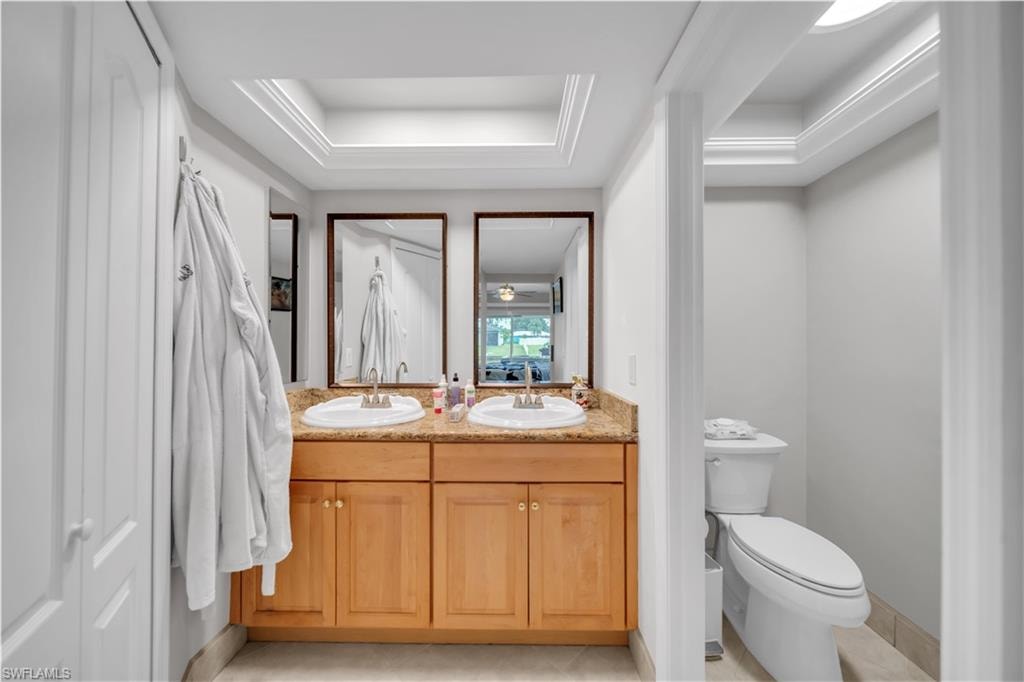 Bathroom with double vanity, a raised ceiling, and light tile patterned flooring