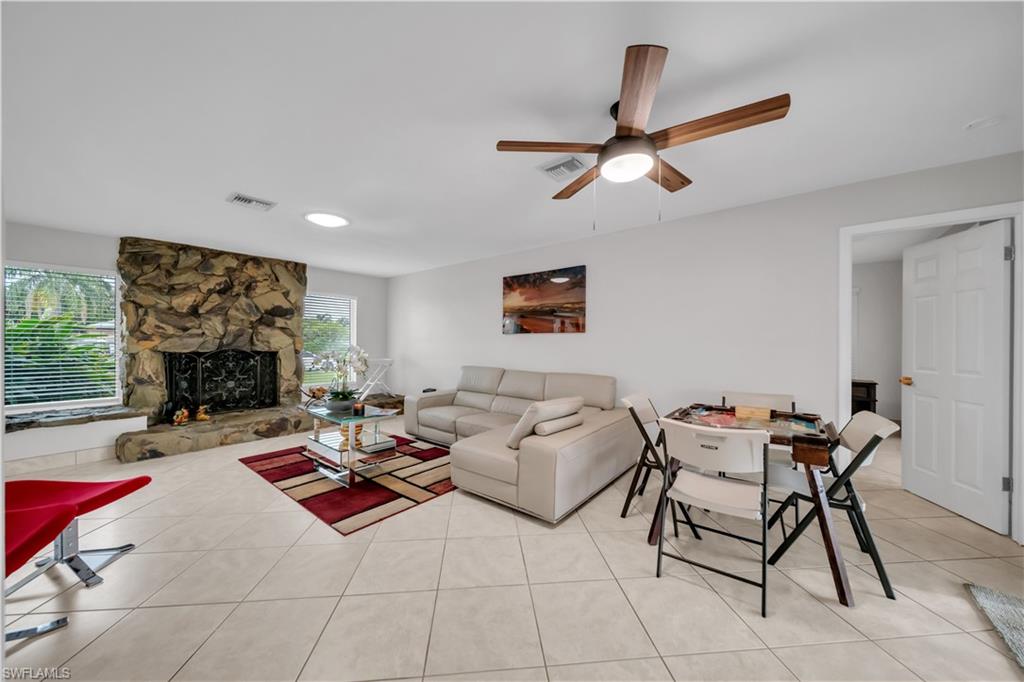 Living room with light tile patterned floors, a stone fireplace, and ceiling fan