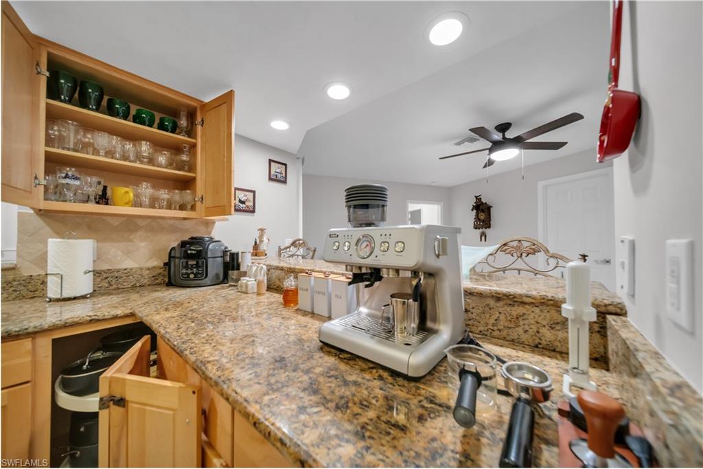 Kitchen with tasteful backsplash, light stone countertops, open shelves, recessed lighting, and light brown cabinets