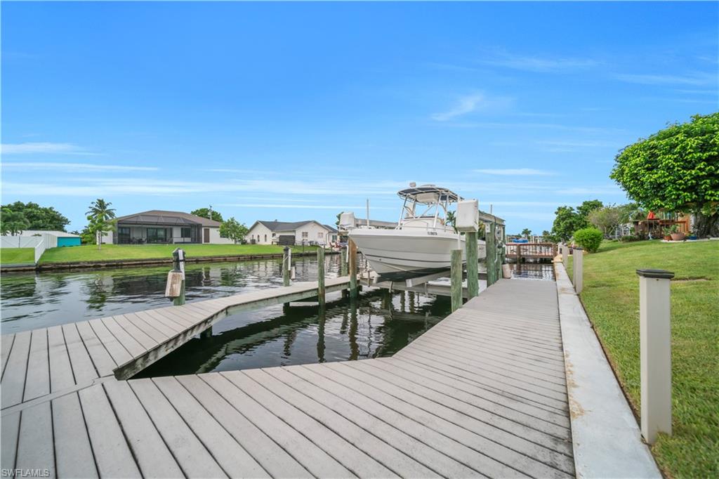 Dock area featuring boat lift, a water view, a yard, and a residential view