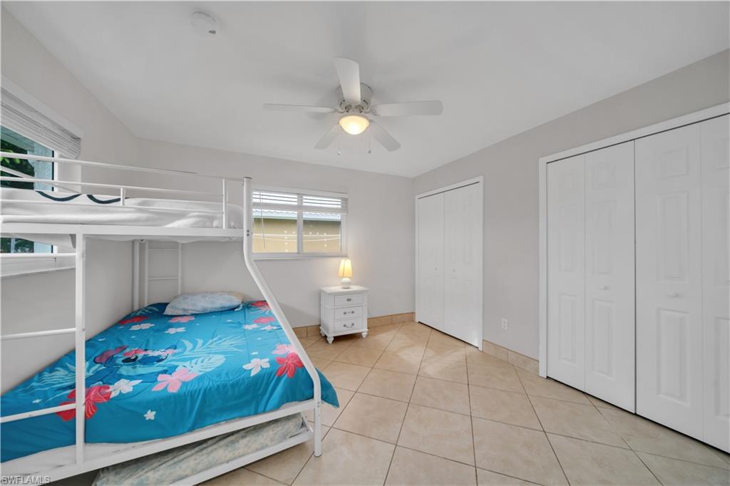 Bedroom with light tile patterned floors, two closets, and ceiling fan