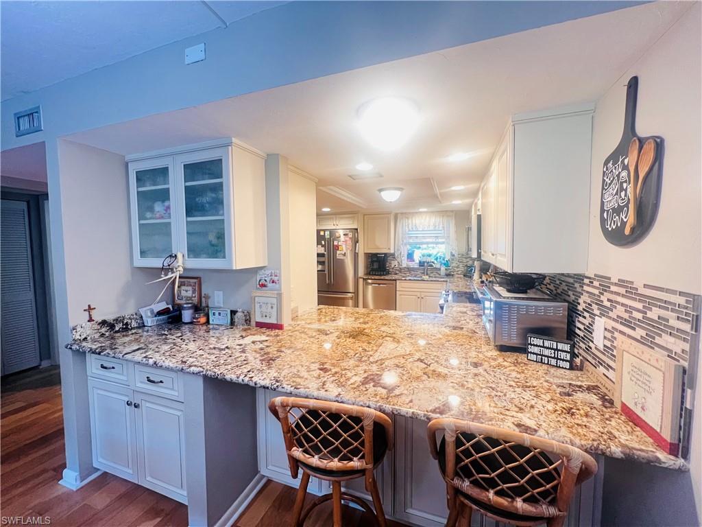 Kitchen with stainless steel appliances, kitchen peninsula, wood-style floors, white cabinets, and a kitchen bar