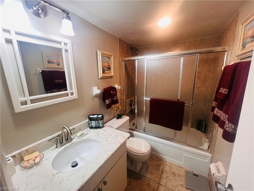 Full guest bathroom with shower / bath combination with glass door, vanity, tile flooring