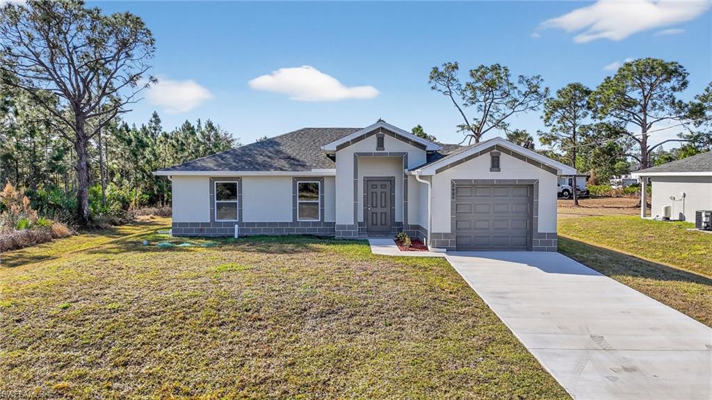 View of front facade featuring stucco siding, a front yard, concrete driveway, an attached garage, and a shingled roof