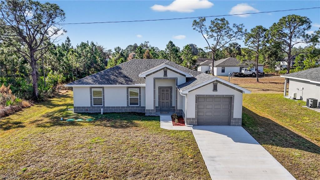 View of front facade featuring stucco siding, a front lawn, concrete driveway, a shingled roof, and a garage