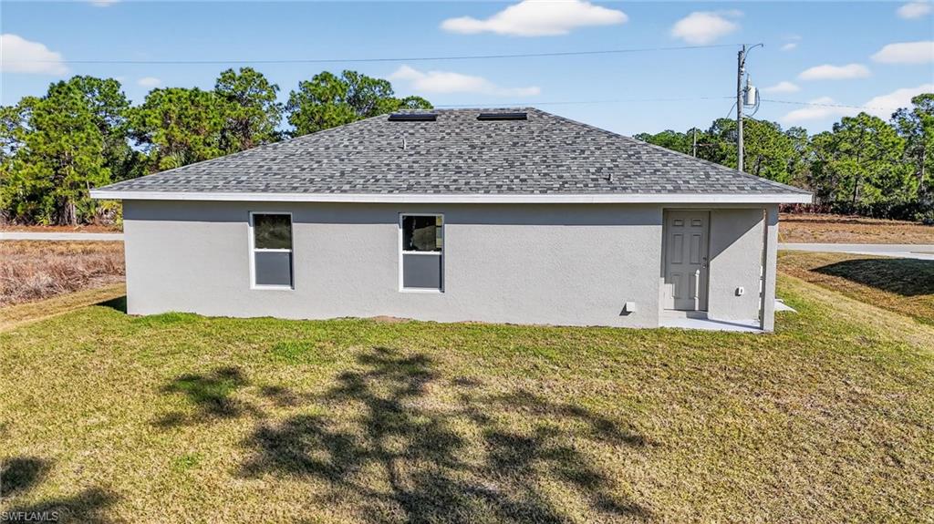 View of home's exterior featuring roof with shingles, a lawn, and stucco siding