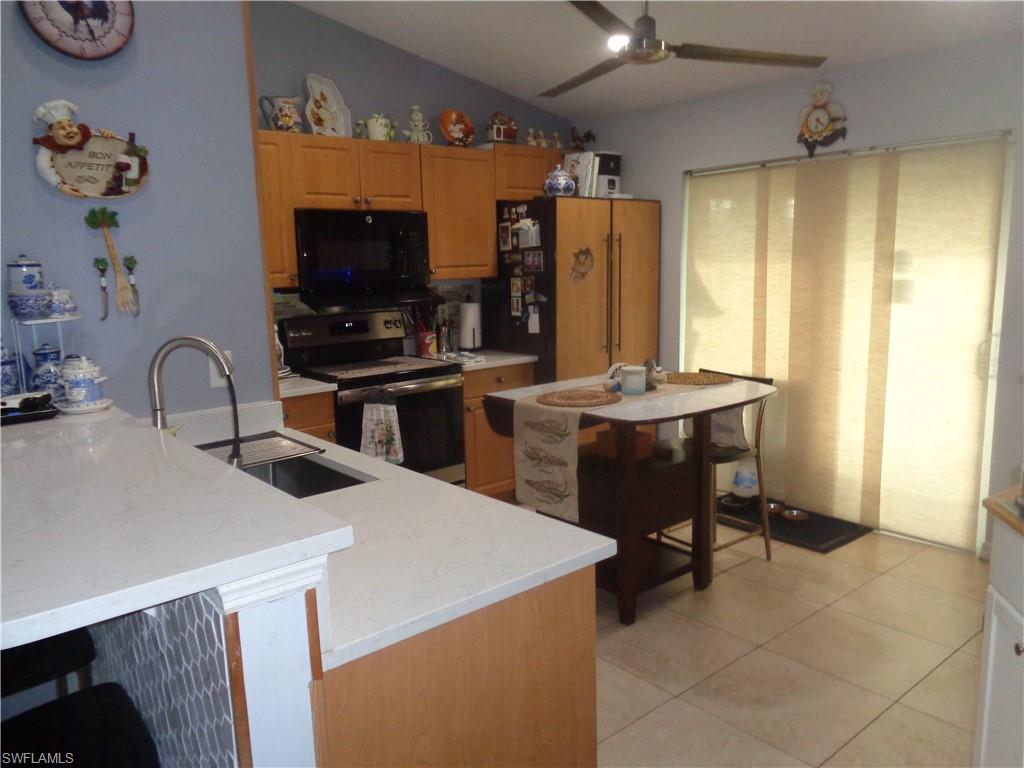 Kitchen featuring stainless steel range with electric stovetop, black microwave, light tile patterned floors, a ceiling fan, and light stone countertops
