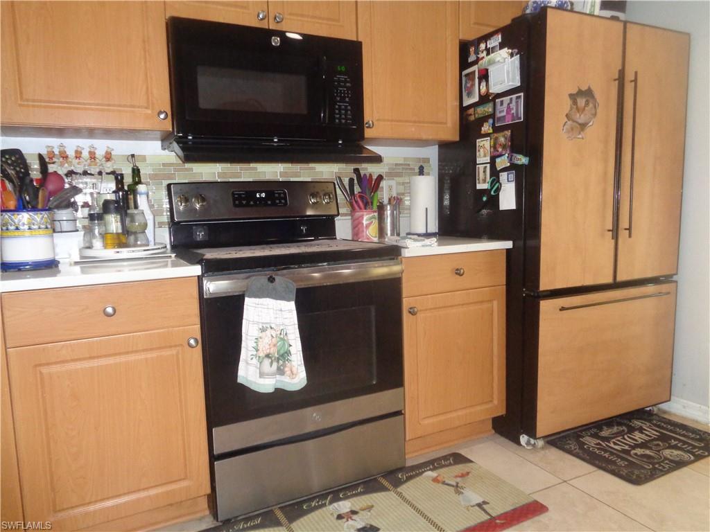 Kitchen featuring stainless steel electric range, black microwave, freestanding refrigerator, backsplash, and light countertops